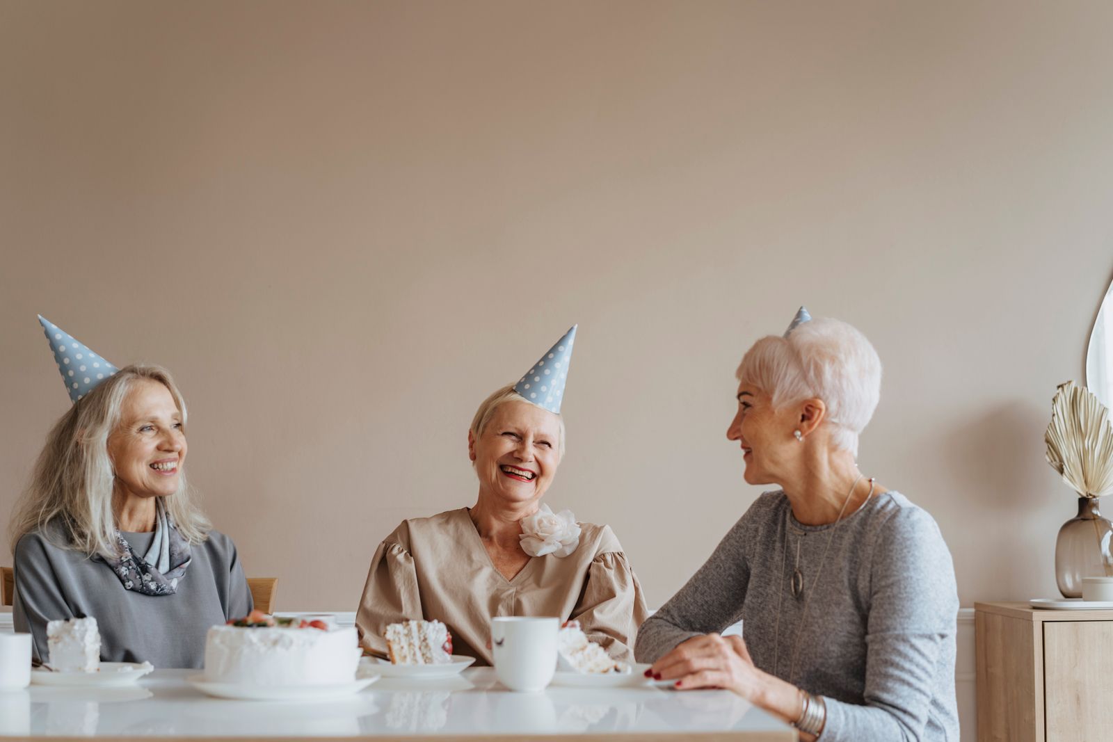 Drei ältere Frauen feiern gemütlich bei Kaffee in einer hellen Wohnung
