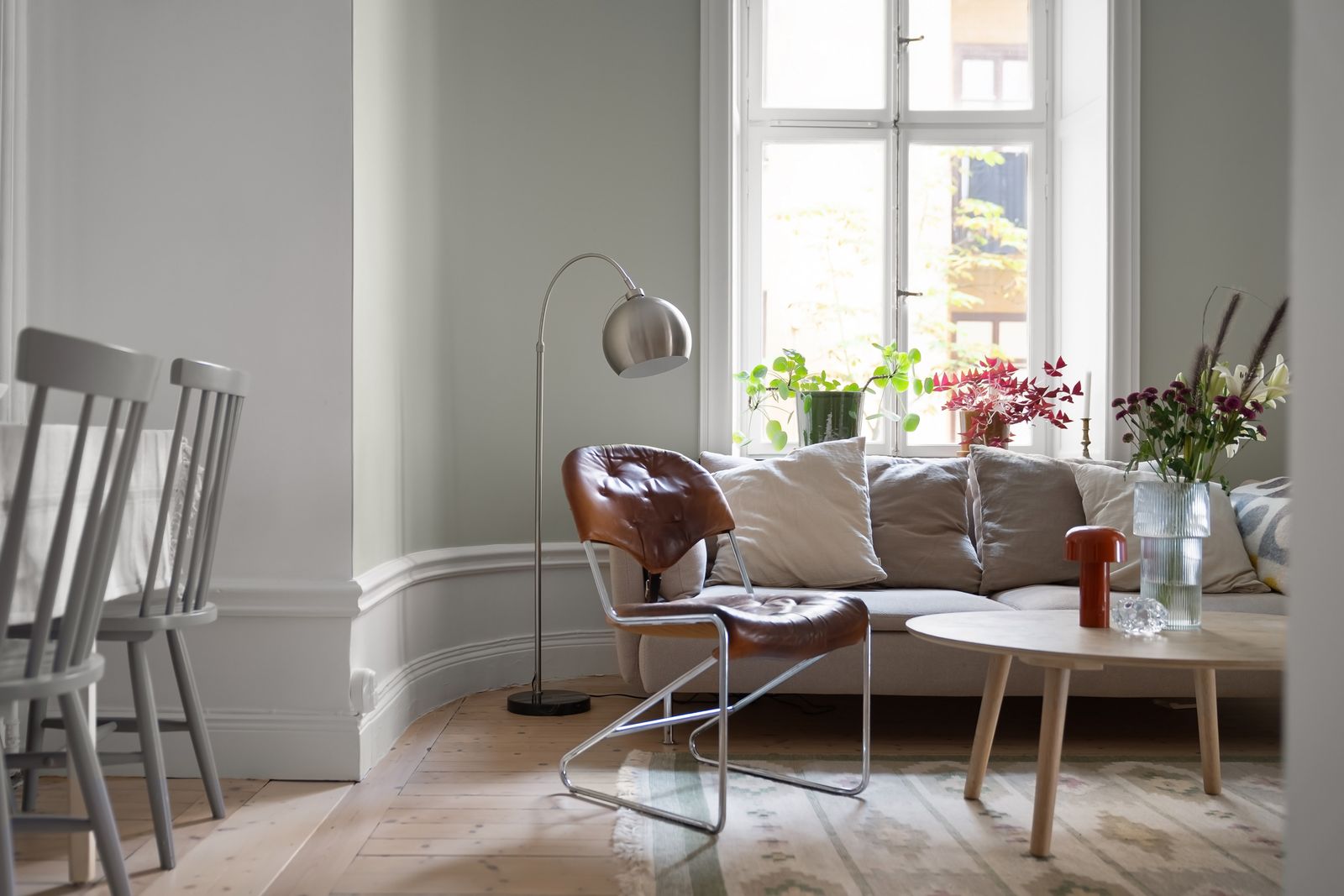 Helles Wohnzimmer mit durchgehendem Holzboden, Stehlampe und viel Tageslicht durch große Fenster