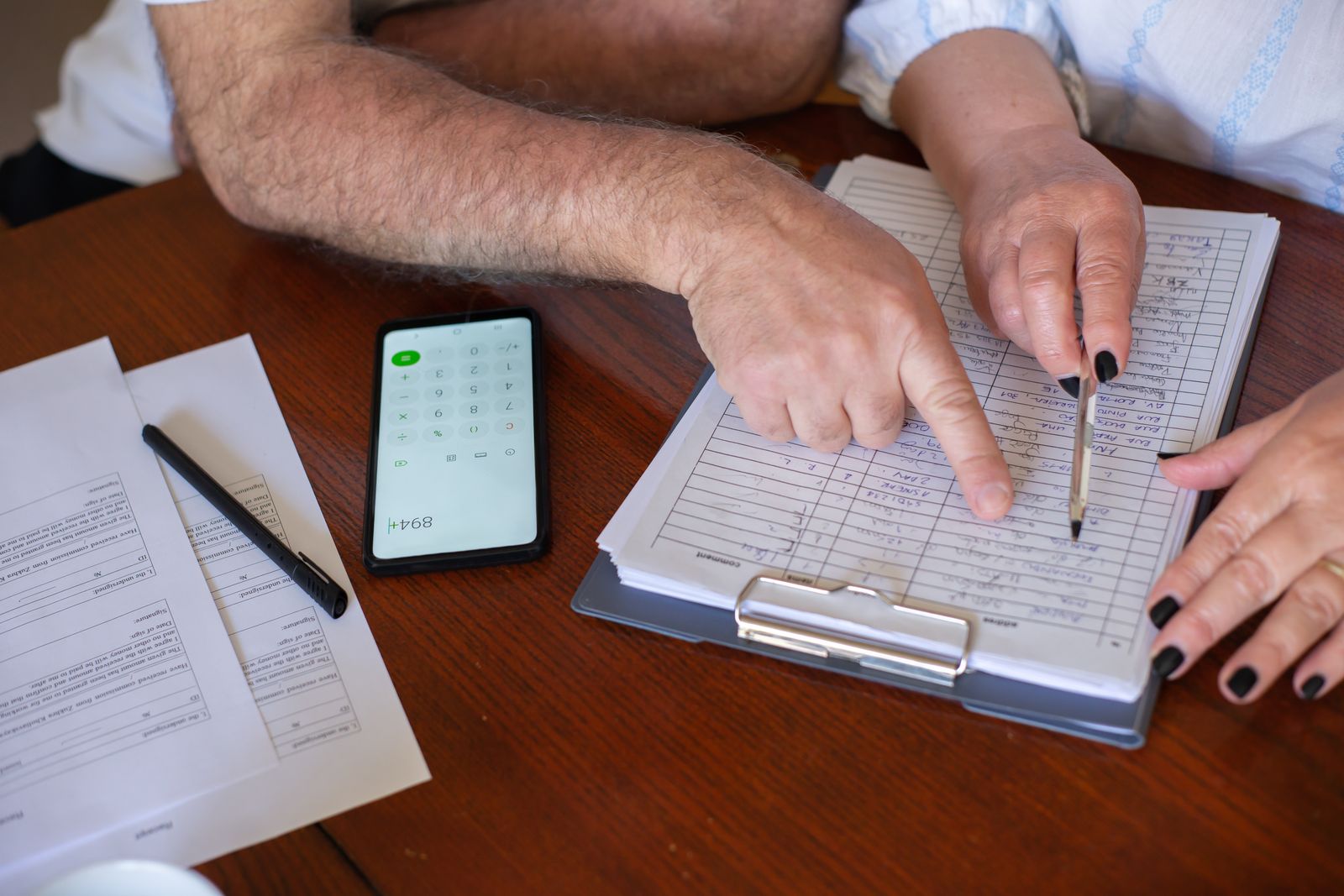 Hände mit Unterlagen und Smartphone bei der Finanzplanung am Tisch