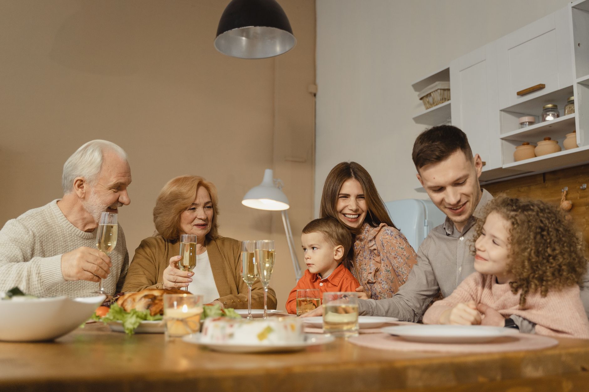 Drei Generationen einer Familie sitzen beim Mehrgenerationenwohnen gemeinsam am Esstisch und lachen miteinander
