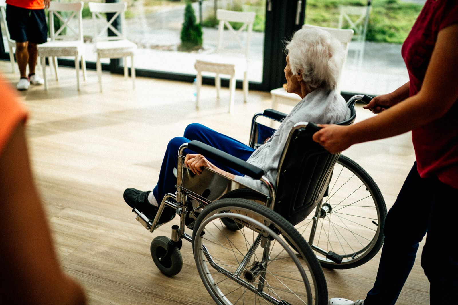 Pflegerin begleitet einen älteren Menschen im Rollstuhl durch ein freundliches Pflegeheim