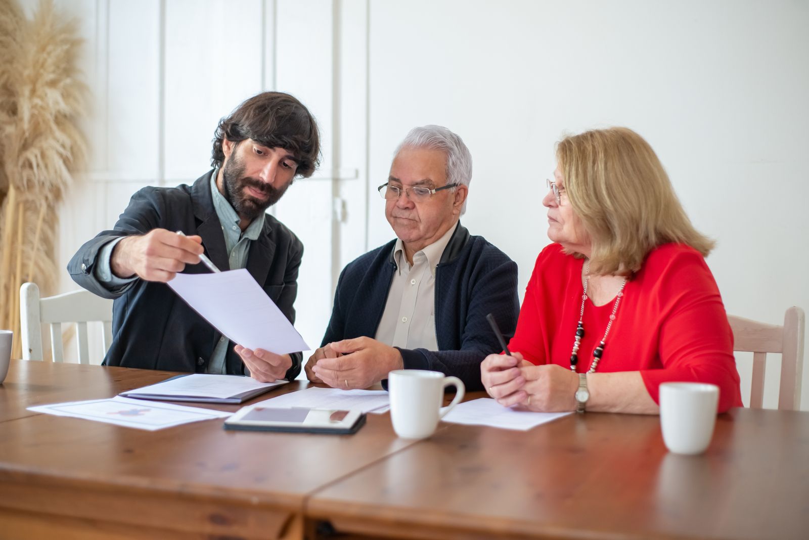 Älteres Paar bespricht mit einem Berater Unterlagen zu Pflegekosten und Immobilienverkauf am Tisch
