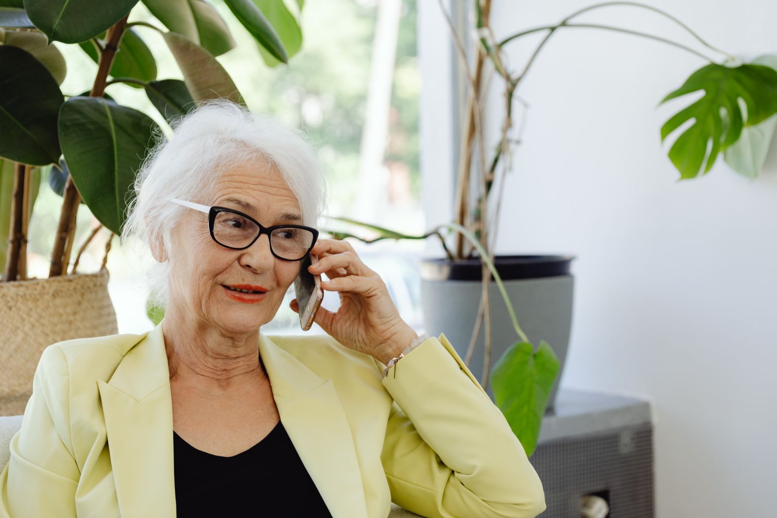 Ältere Dame im hellen Wohnzimmer telefoniert freundlich