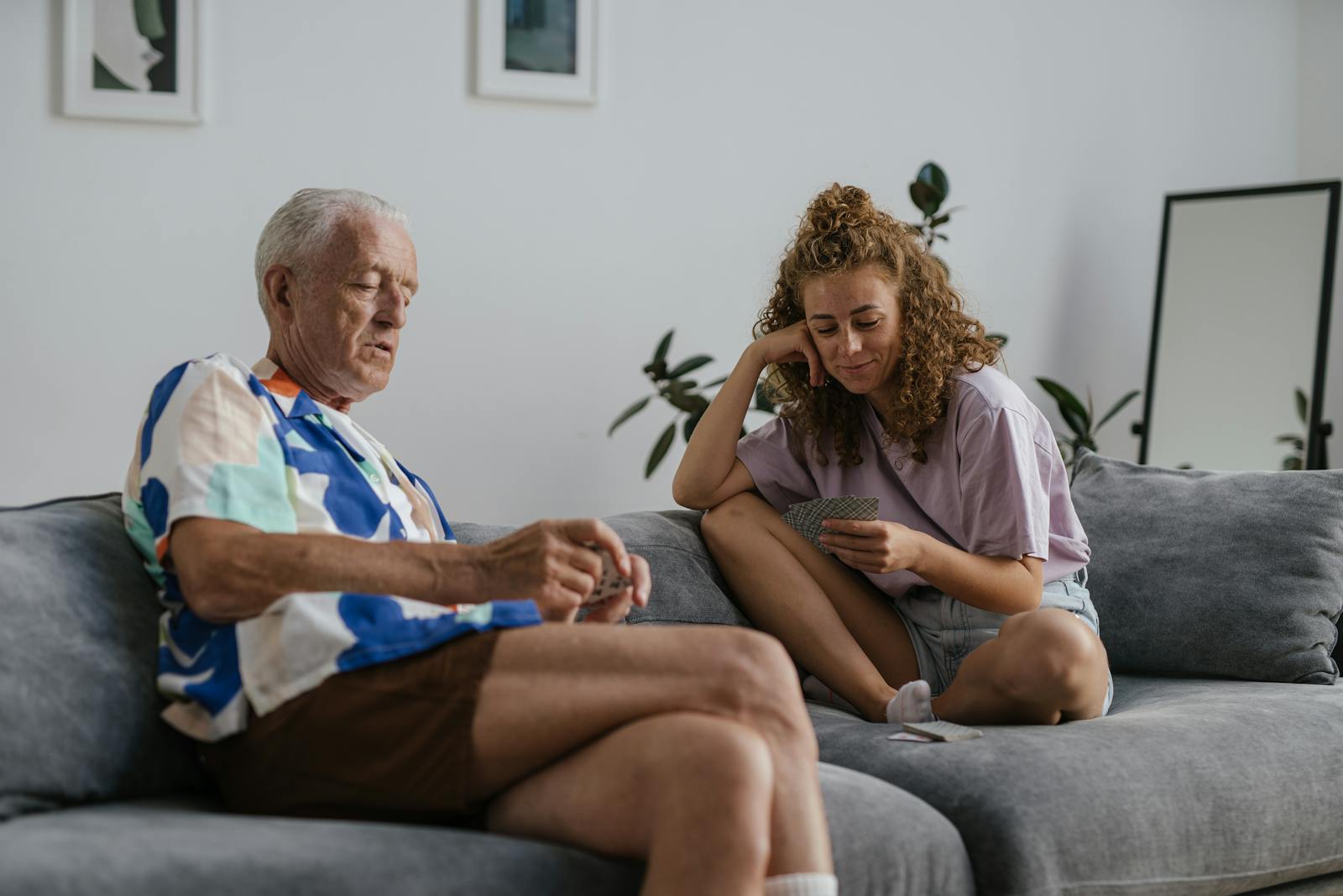 Jüngere Begleiterin spielt mit einem älteren Mann auf dem Sofa Karten