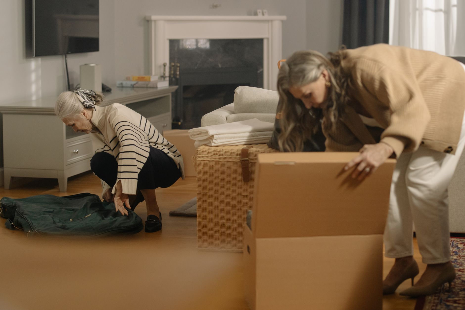 Ältere Frau packt gemeinsam mit einer Angehörigen Umzugskartons im Wohnzimmer für den Umzug ins Pflegeheim